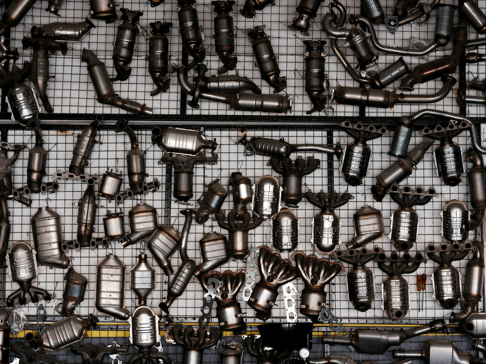 Many catalytic converters hanging on a grid wall.